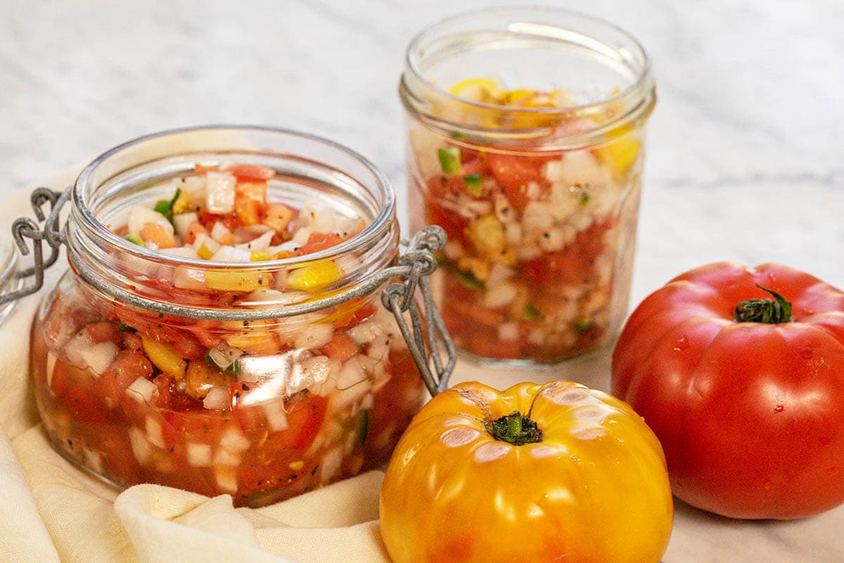 Whole ripe tomatoes sitting beside jars of relish.