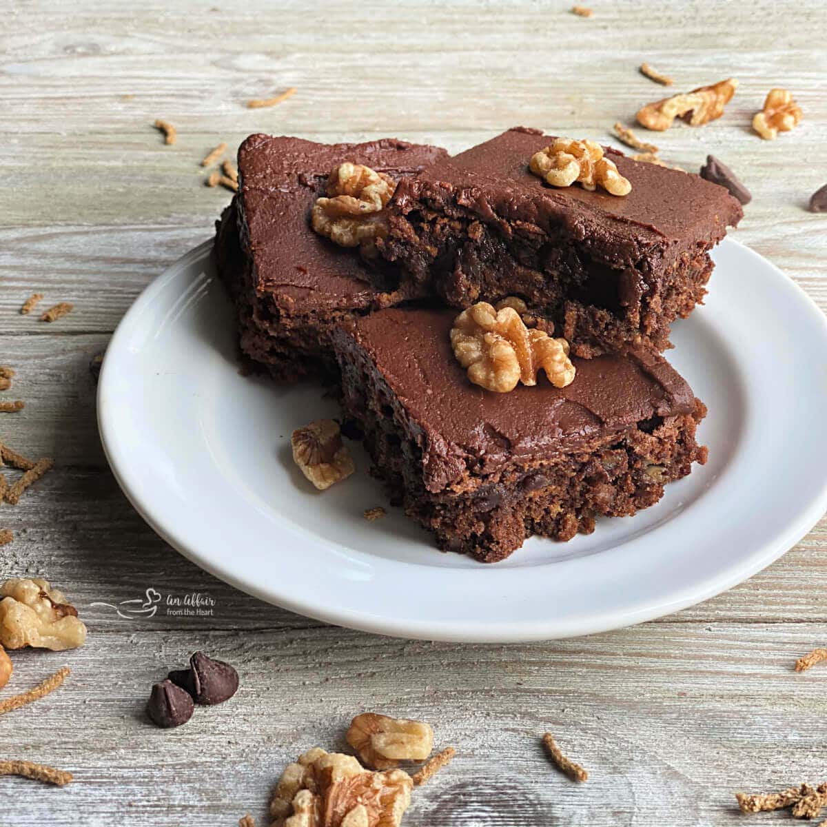 Three chocolate banana bars on a white place surrounded by nuts.