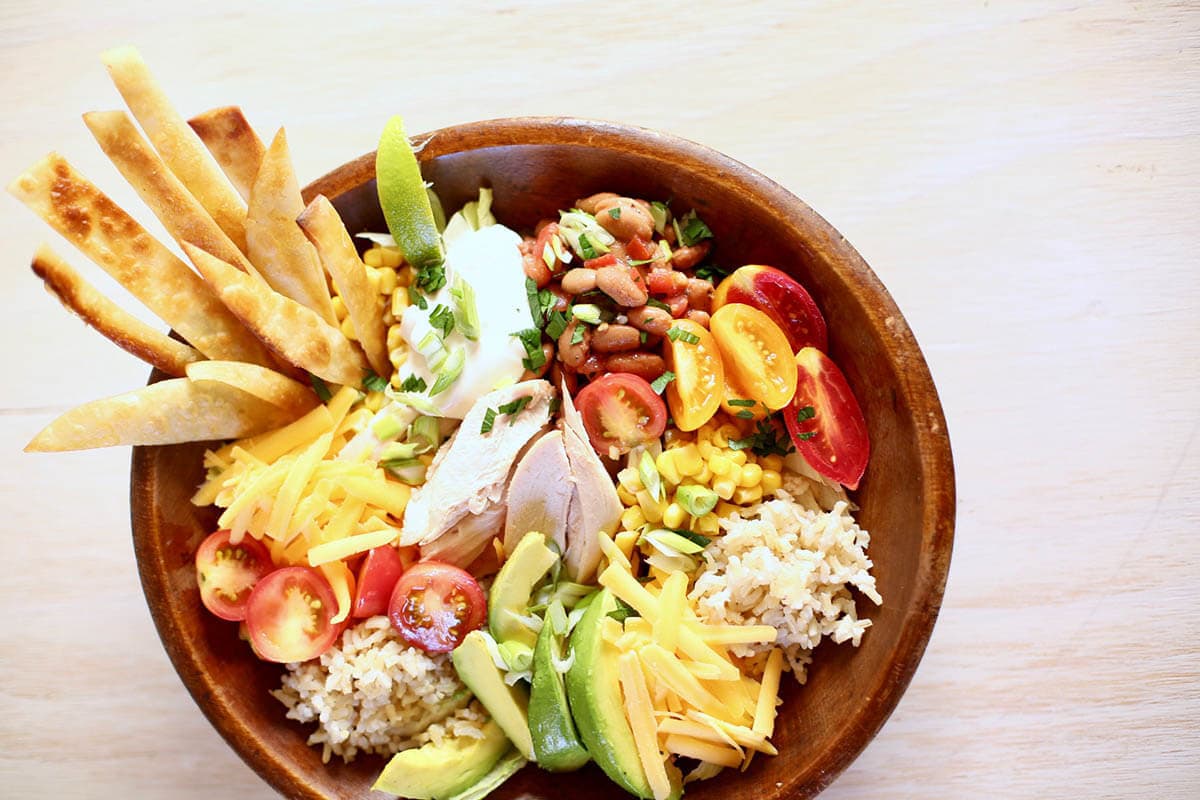 Rotisserie Chicken Burrito Bowl with lettuce, avocado, tomatoes and tortilla strips.