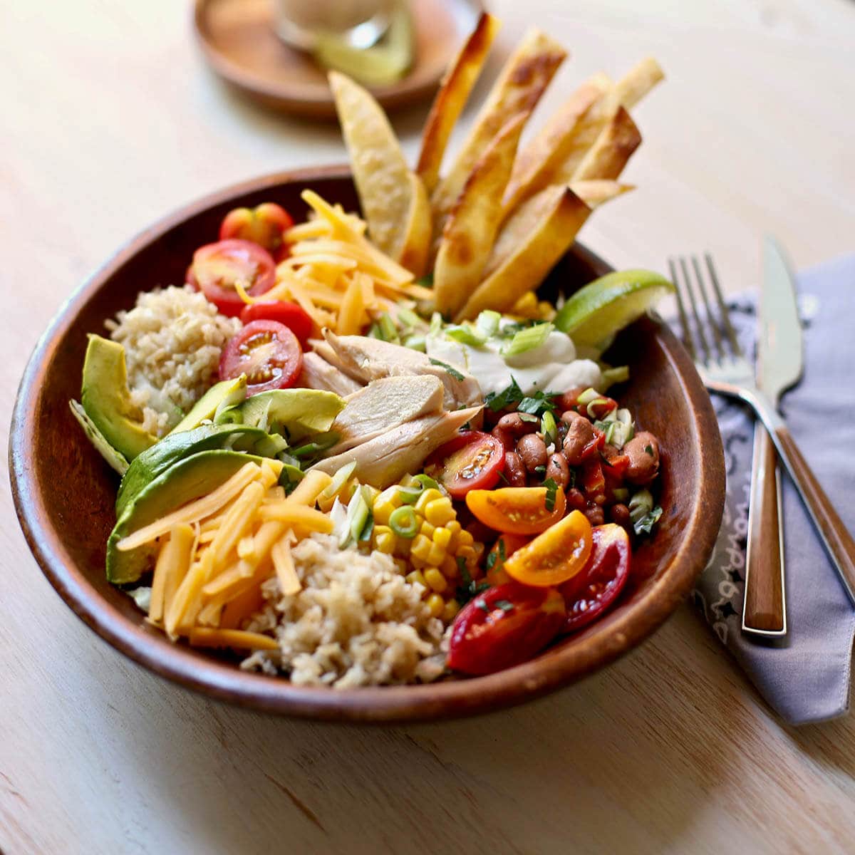 Big salad with lettuce, rice, chicken, cheese and tortilla strips in bowl.