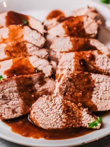 Sliced Pork Tenderloin on platter drizzled with balsamic glaze.