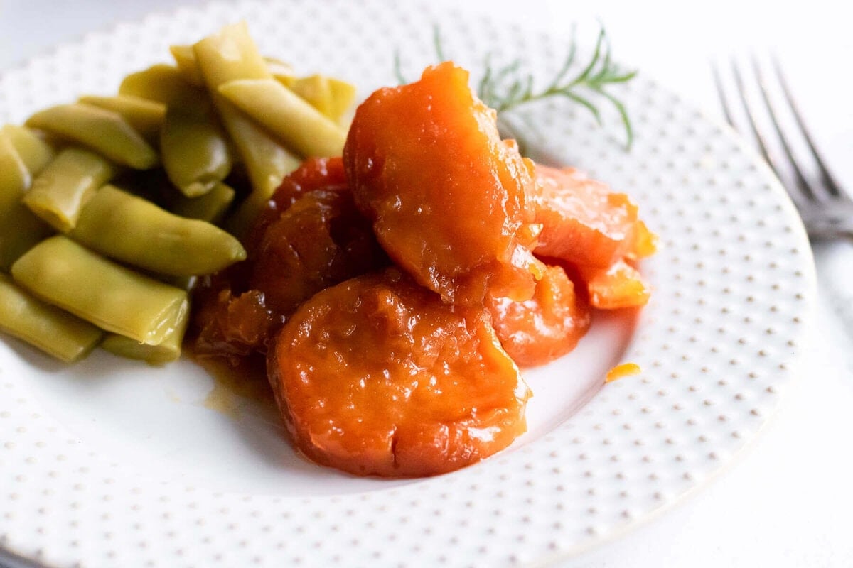 Candied Sweet Potatoes on white plate served with a side of green beans.