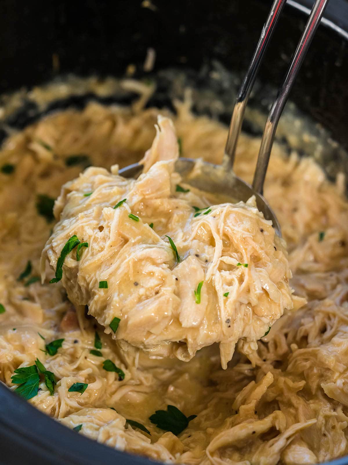 Shredded Chicken with Gravy in crockpot with a big ladle grabbing a scoop.