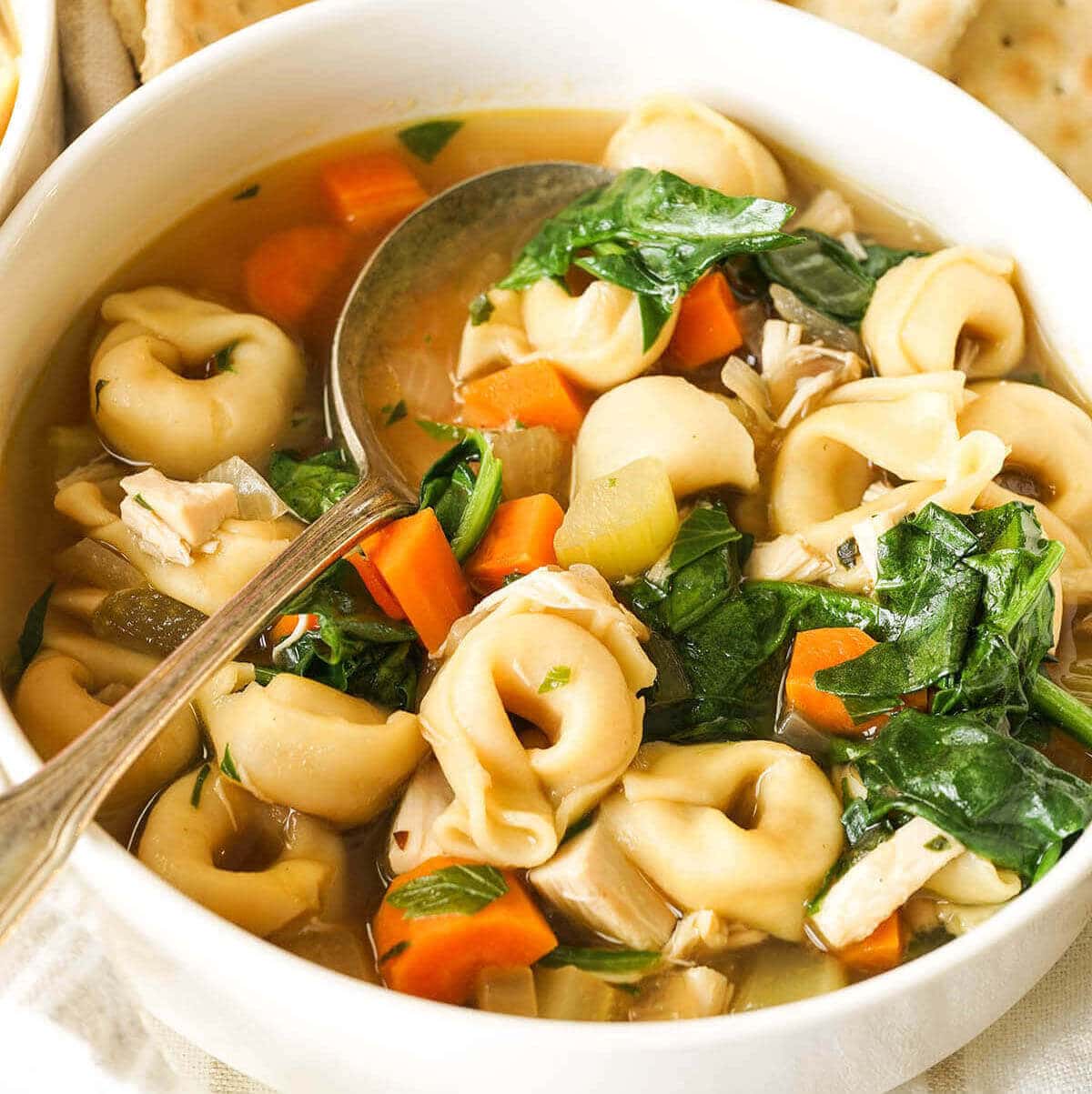 A white bowl filled with chicken tortellini soup with spoon.  