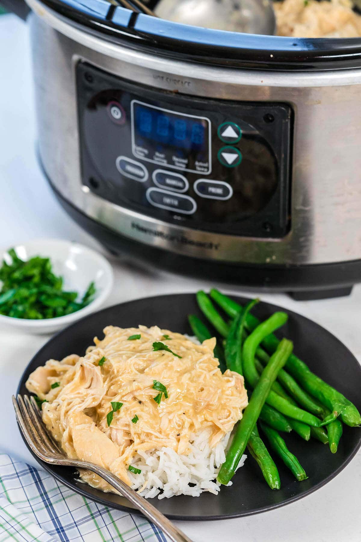 Crockpot filed with Chicken and Gravy beside a plate with rice topped with chicken and served with green beans.