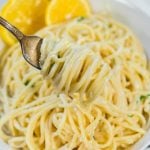 Lemon Garlic Pasta twirled around a fork with a bowl of pasta in the background, served with slices of fresh lemon.