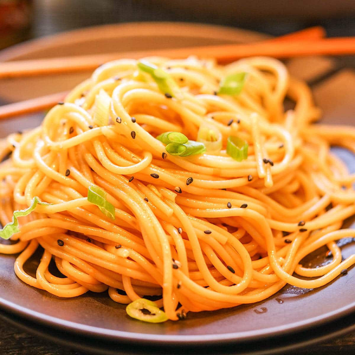 Spicy Sesame Noodles on plate with chopsticks. They are topped with thinly sliced green onions and black sesame seeds.