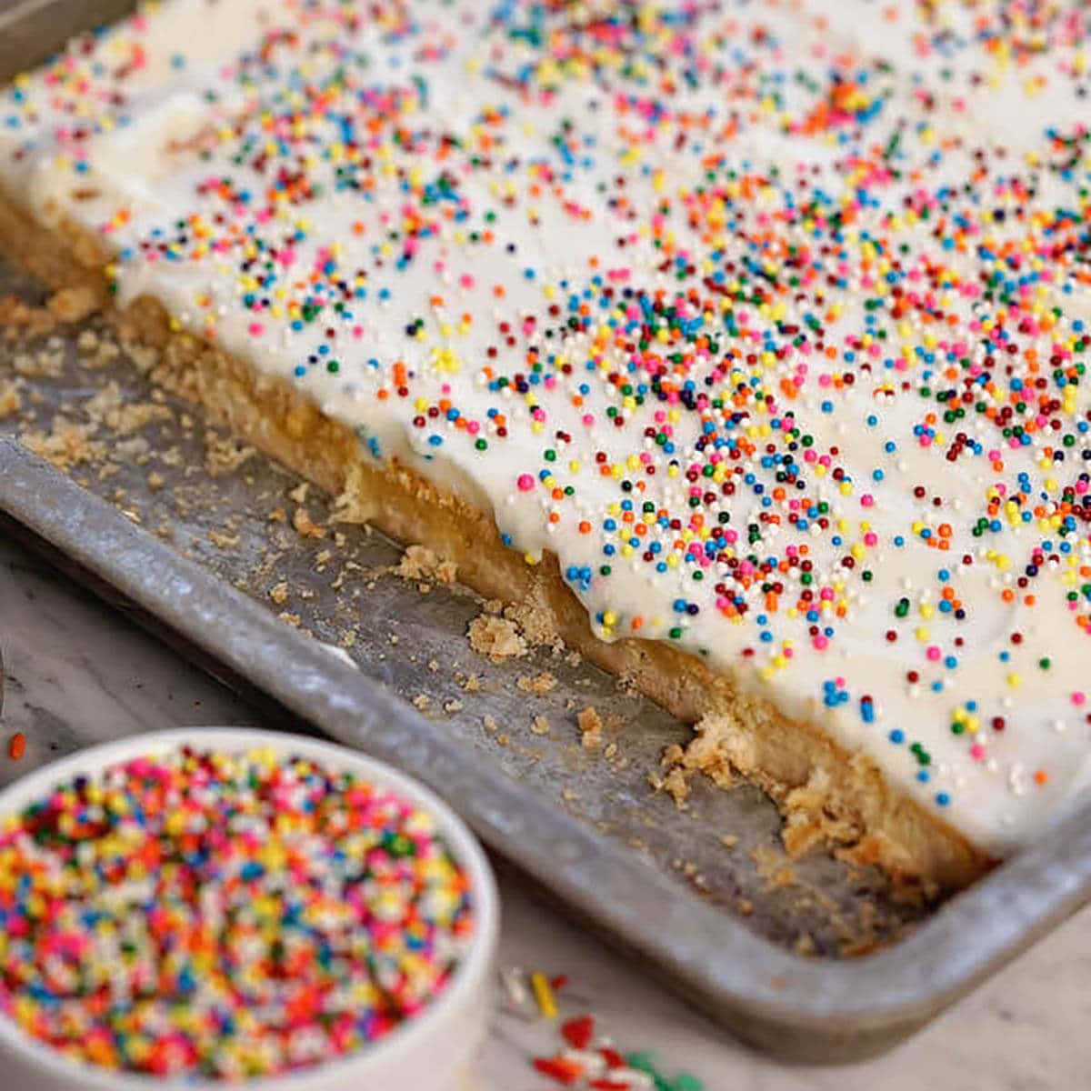 Lemon bars in a sheet pan topped with a cream cheese frosting and sprinkles 