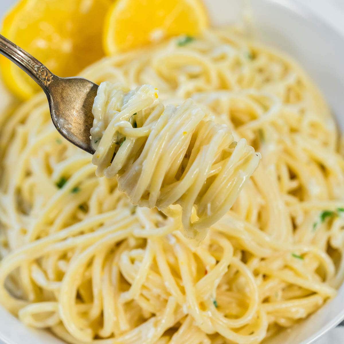 A bowl of lemon pasta served with slices of lemon. A fork has twirled a big serving around it, ready to eat!