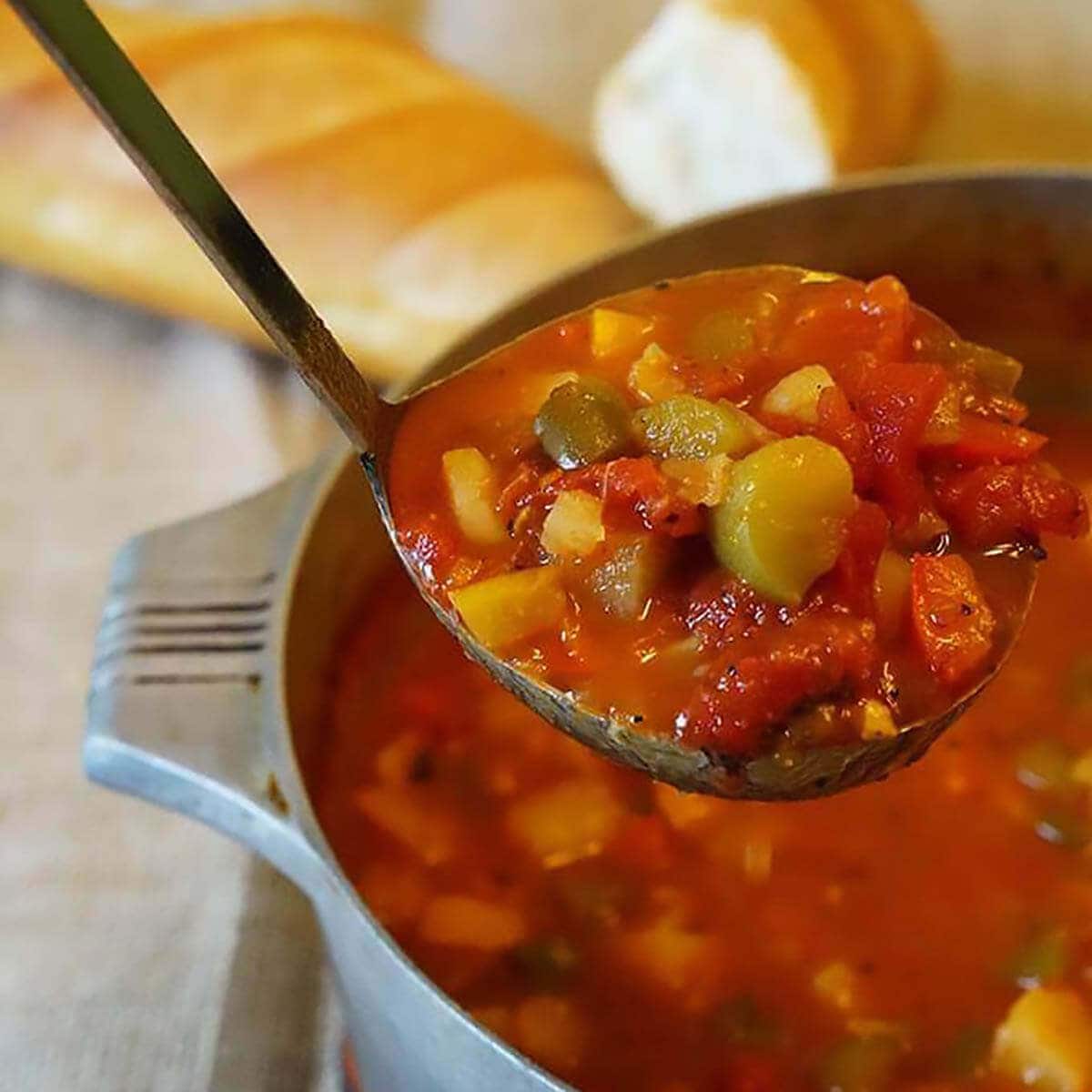 Italian pepper stew in an aluminum pot with a ladle grabbing a big serving, served with fresh bread.