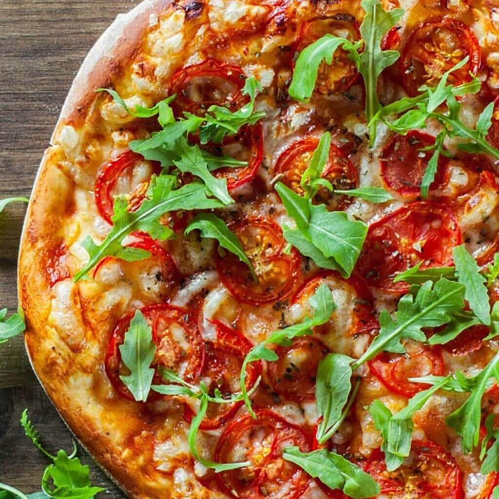 Homemade Pizza topped with tomatoes and arugula 