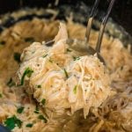 Slow cooker filled with chicken and gravy with ladle of meat.