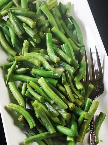 Microwave steamed green beans on white platter with serving fork.