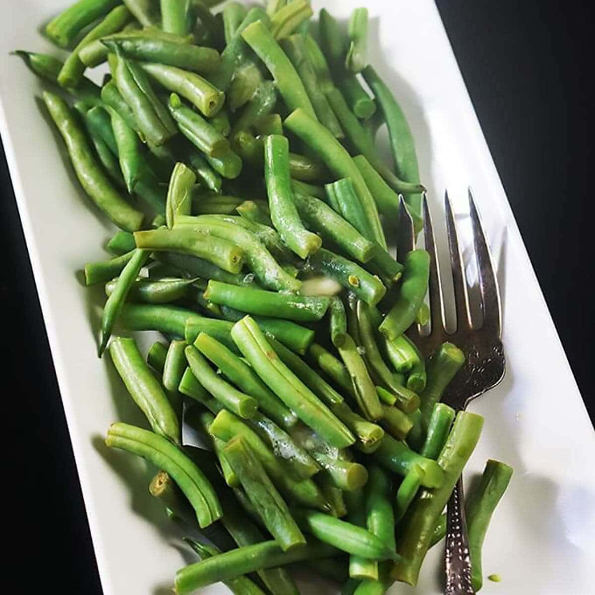 Microwave steamed green beans on white platter with serving fork.