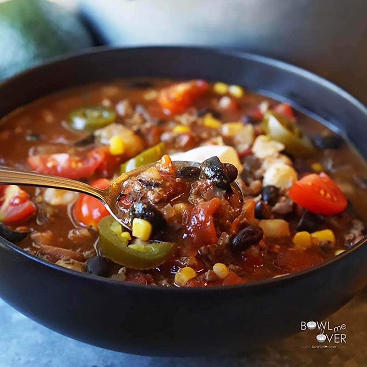 Taco soup in black bowl topped with sour cream, A is used to scoop a big bite. 