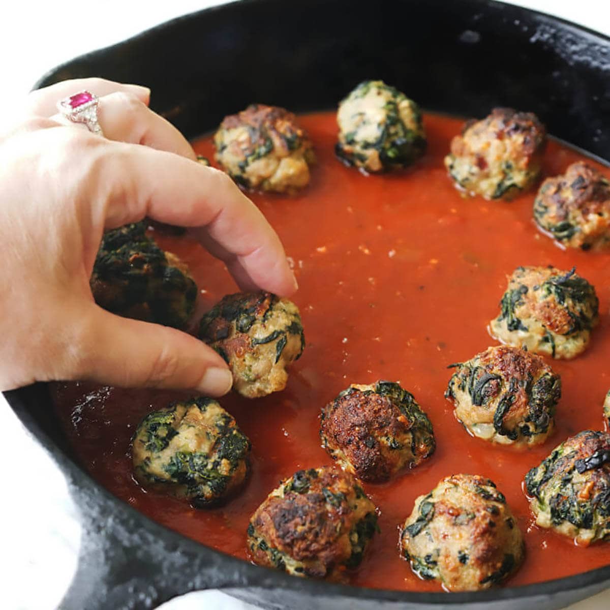 Turkey and spinach meatballs in a skillet with marinara sauce.