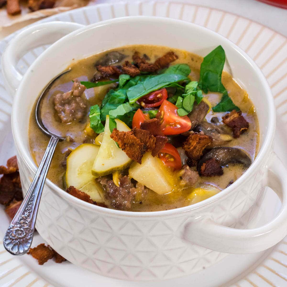 Bacon Cheeseburger Soup in white bowl topped with shredded lettuce, tomatoes and pickles.