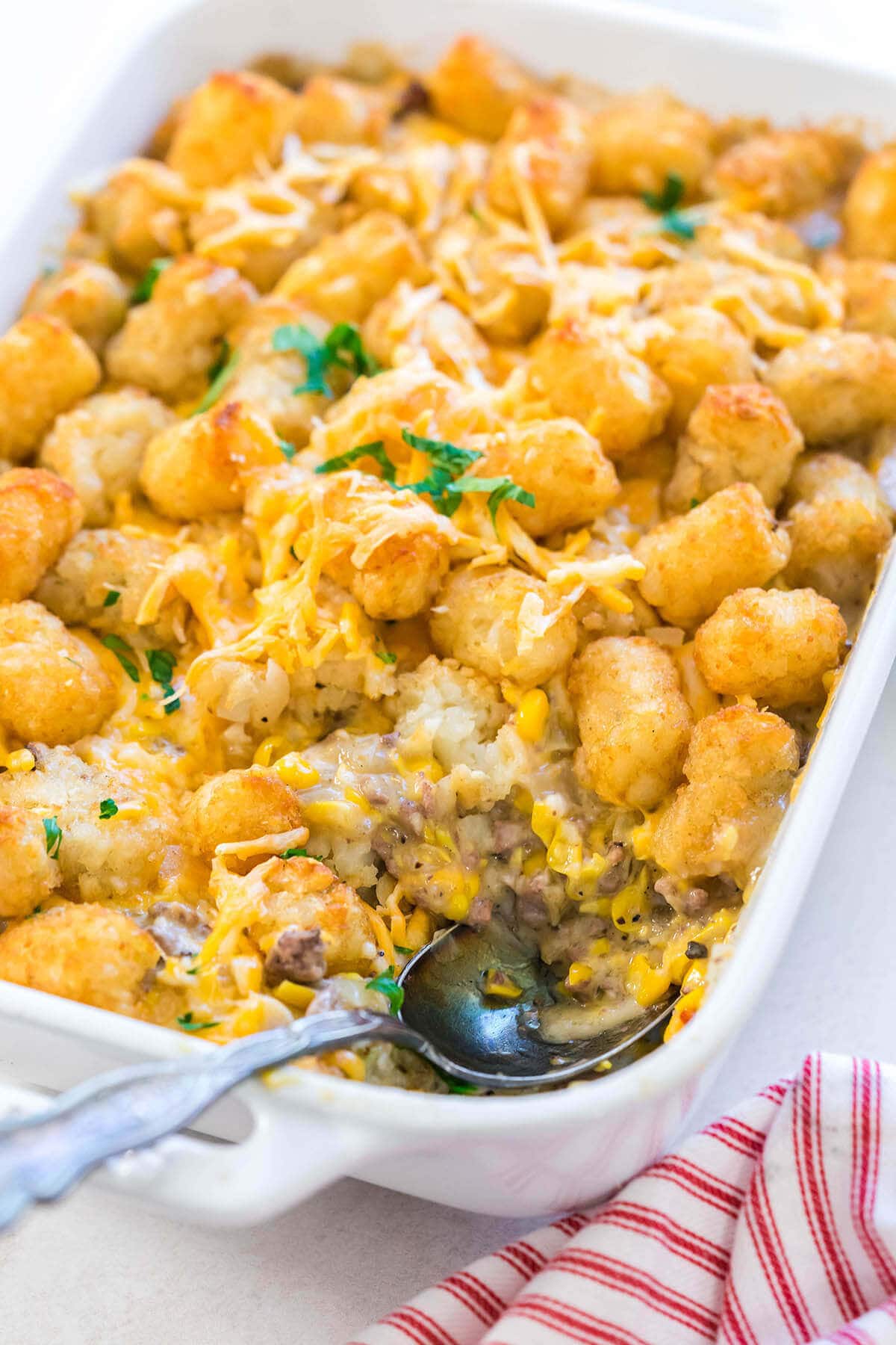 Tater Tot Casserole in white dish with serving spoon.