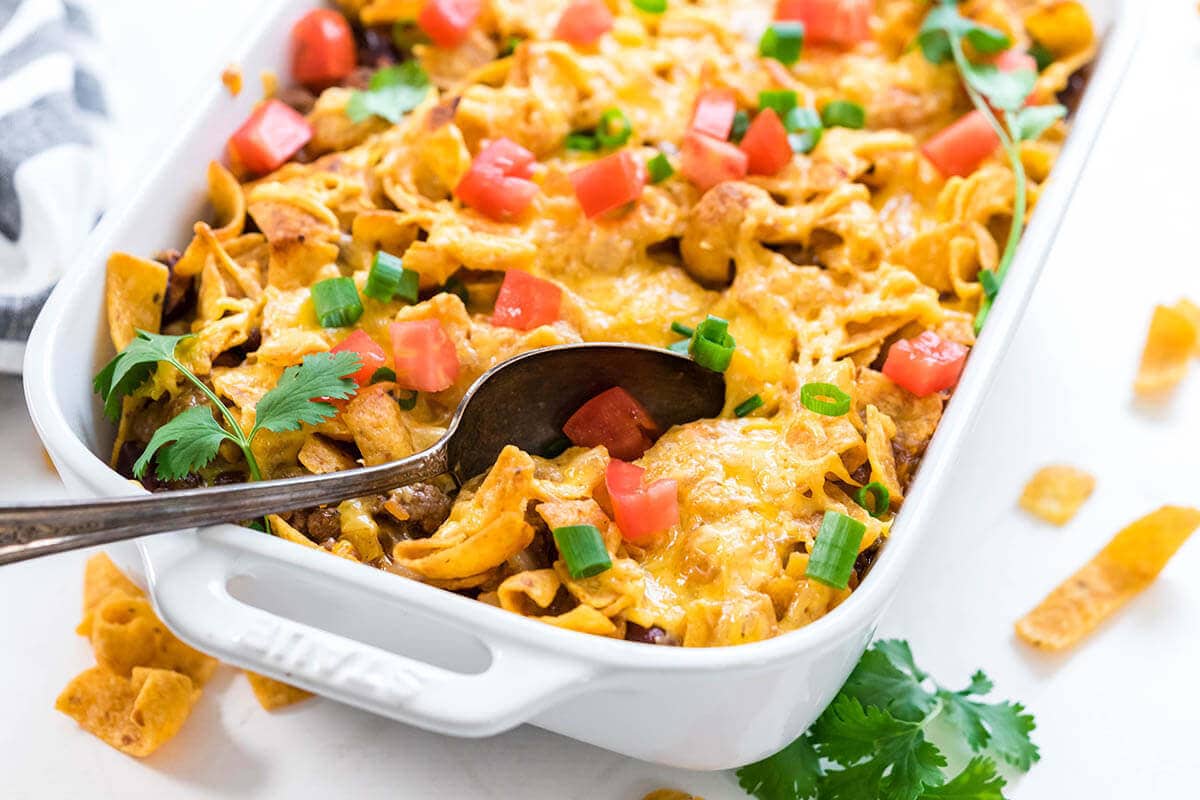 Frito Taco Pie in white casserole dish topping with melted cheese with serving spoon.