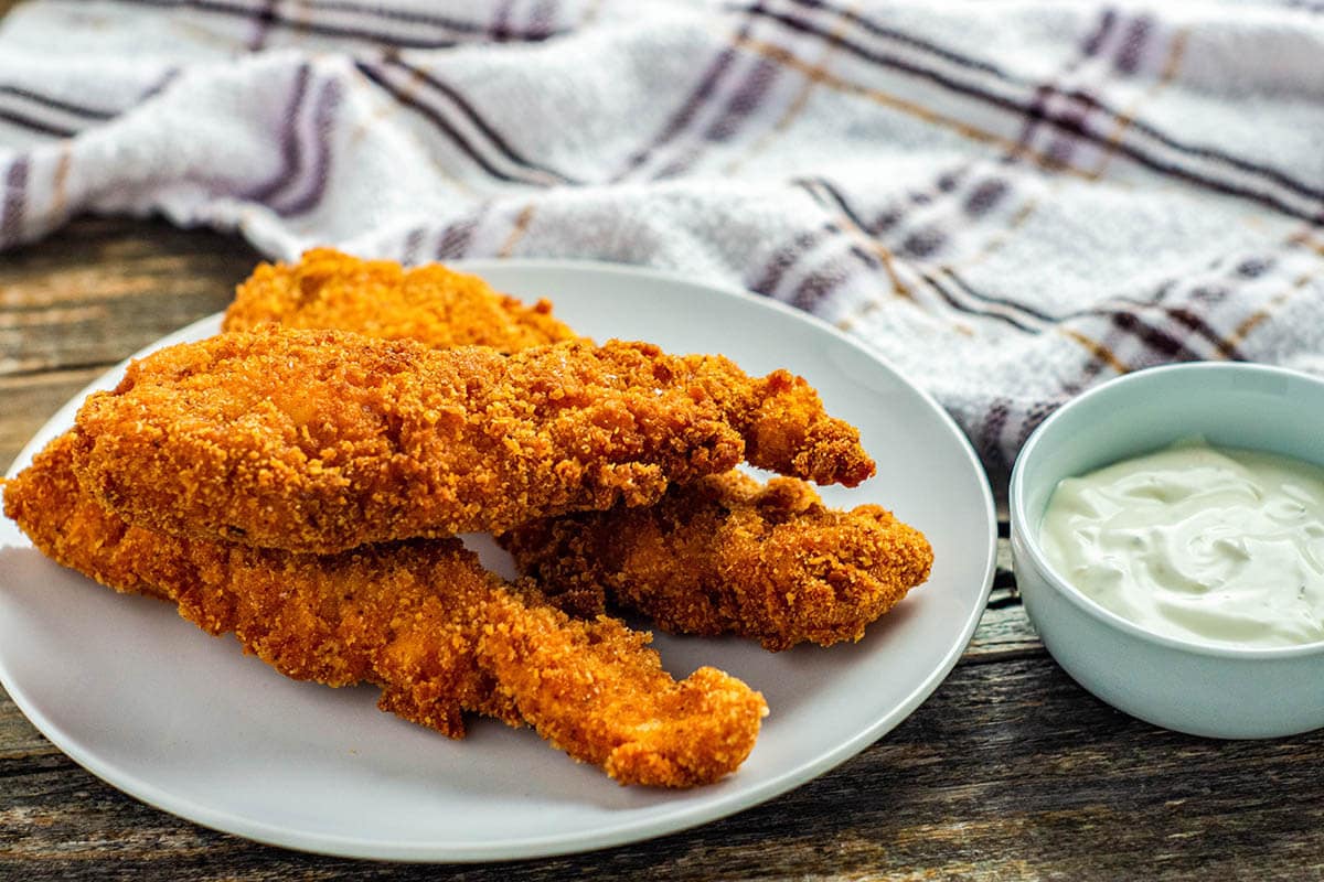 Fried chicken strips on a white plate with dipping sauce. 