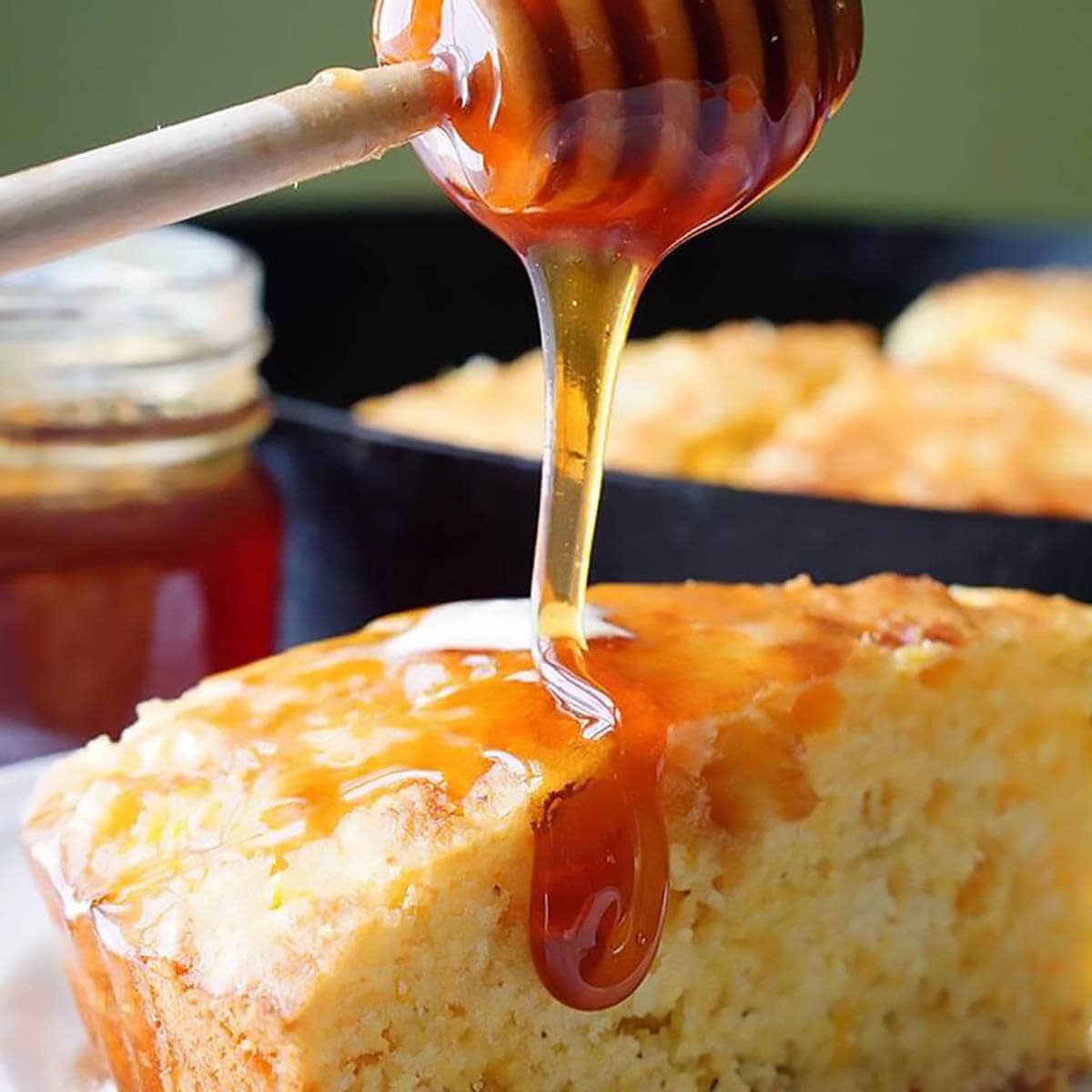 Cornbread with honey being drizzled over the top and sides.