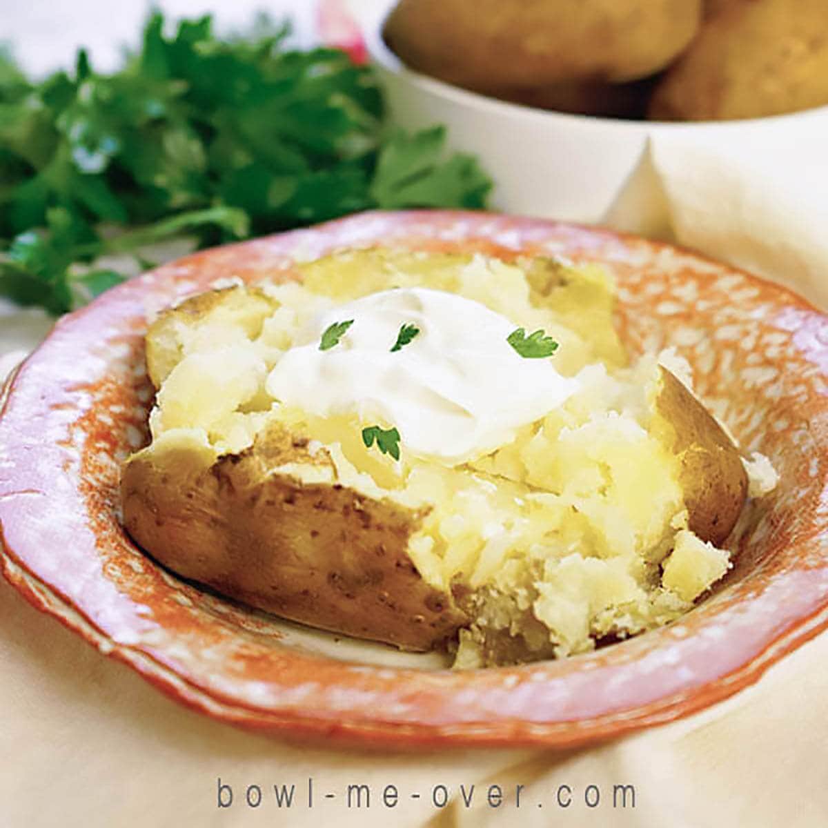 Baked potato in bowl topped with butter, sour cream and chives. 
