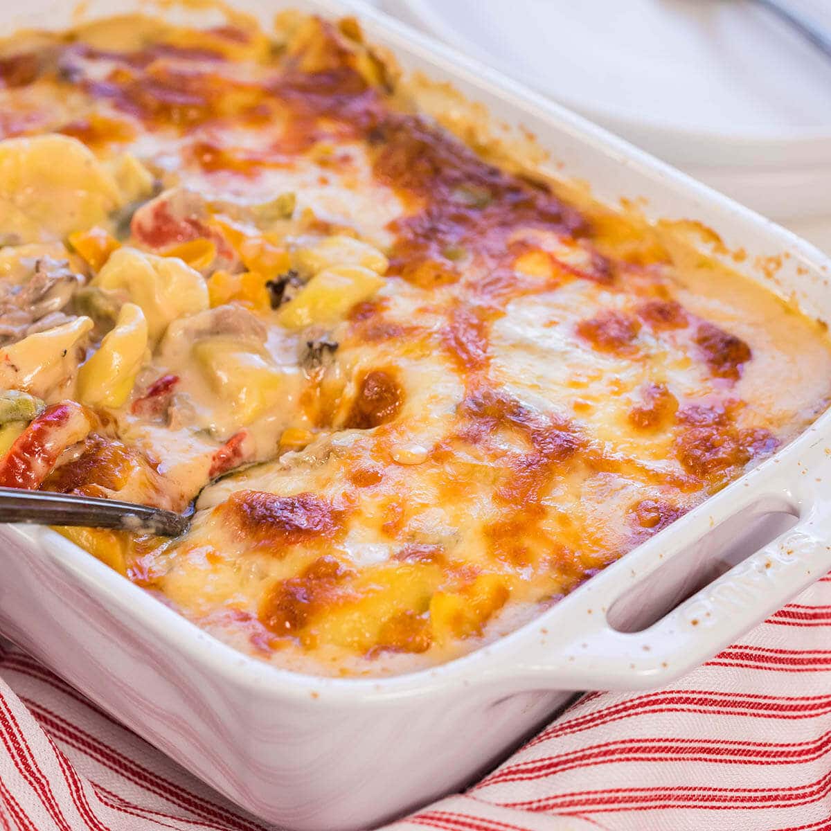 Baked Tortellini in white casserole dish with spoon.