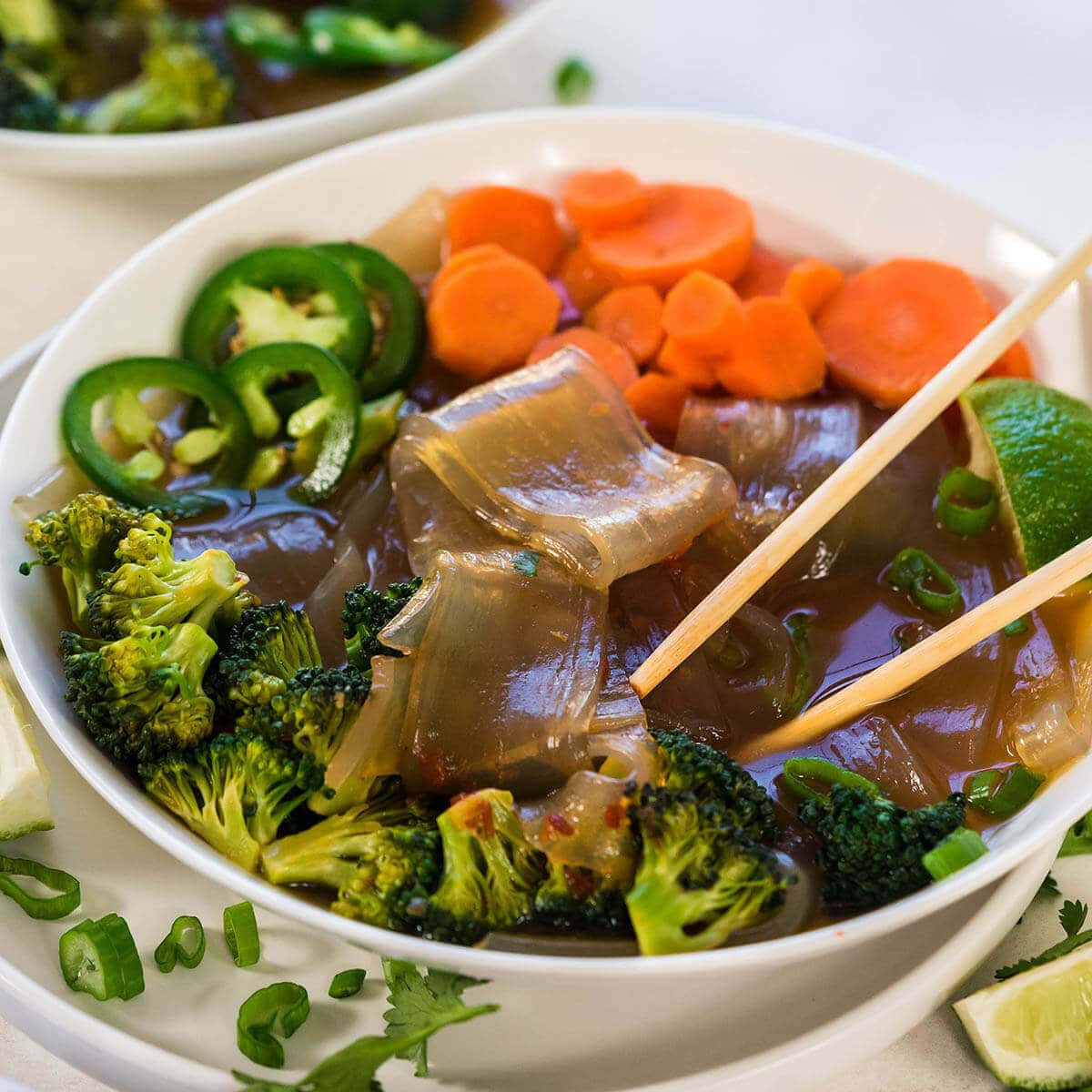 Vegetable soup in white bowl served with chopsticks and garnished with sliced green olives.