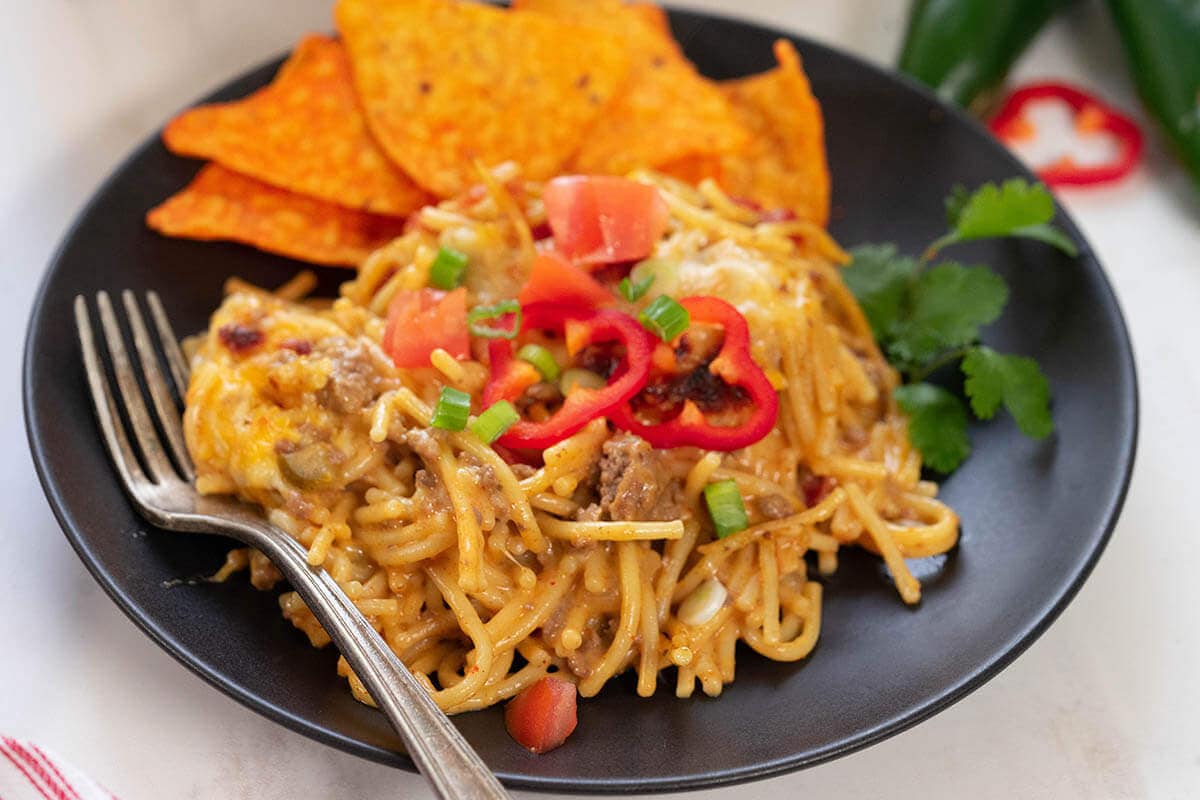 Taco spaghetti served with Doritos chips on black plate with fork.