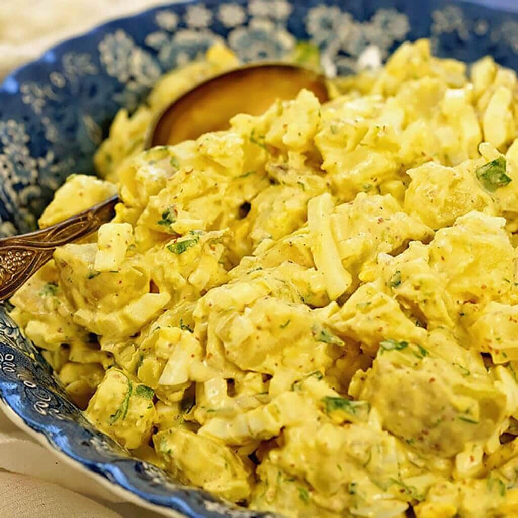 Deviled Egg Potato Salad in blue bowl with serving spoon.
