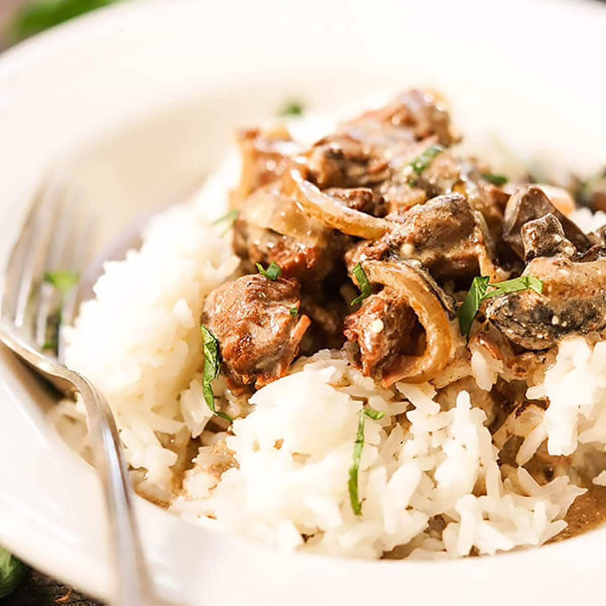 Beef Stroganoff in a white bowl over rice. 
