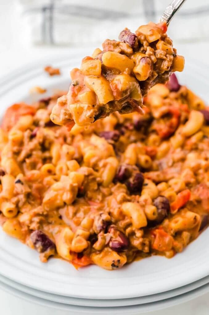 A heaping bowl of cheesy chili Mac n Cheese with a spoon taking a big scoop.