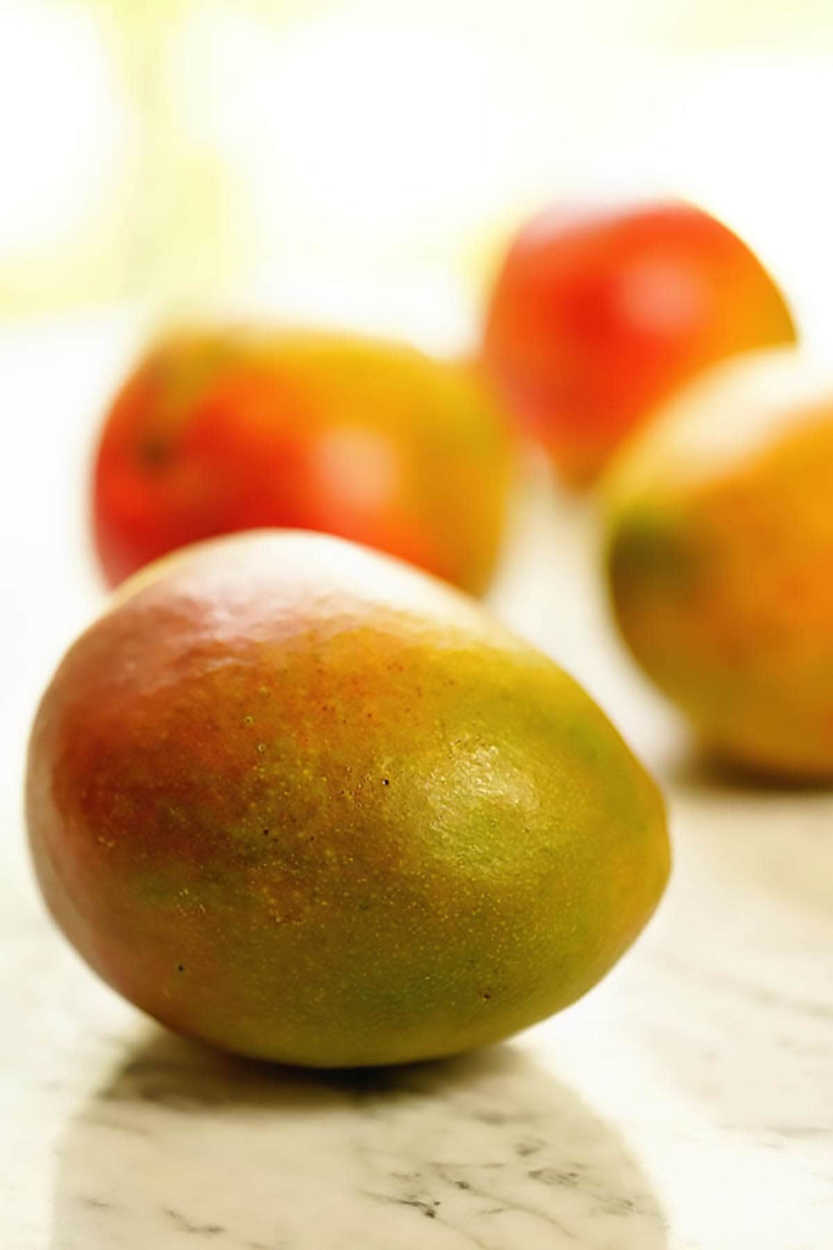 Four ripe mangos on marble slab.