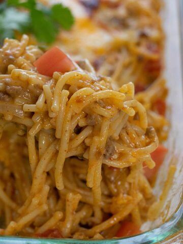 Big spoonful of creamy taco spaghetti with casserole dish.