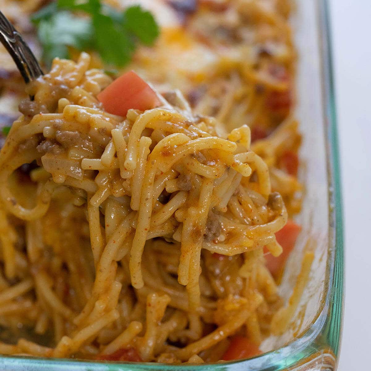 Big spoonful of creamy taco spaghetti with casserole dish.