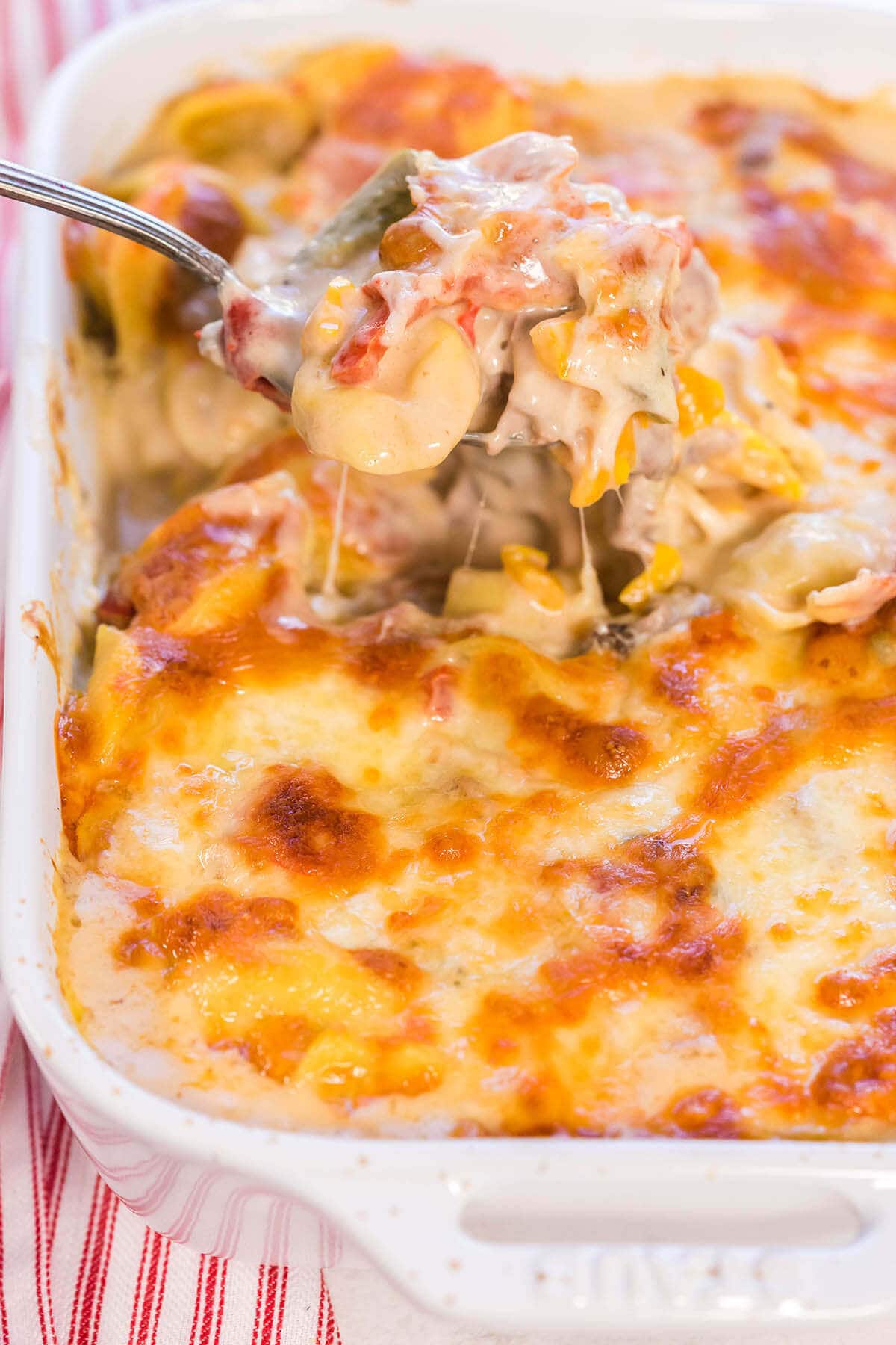 Tortellini pasta bake in casserole dish with serving spoon scooping out a big helping.