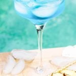 Cocktail on the ledge of a pool garnished with pineapple. With Pinterest overlay.