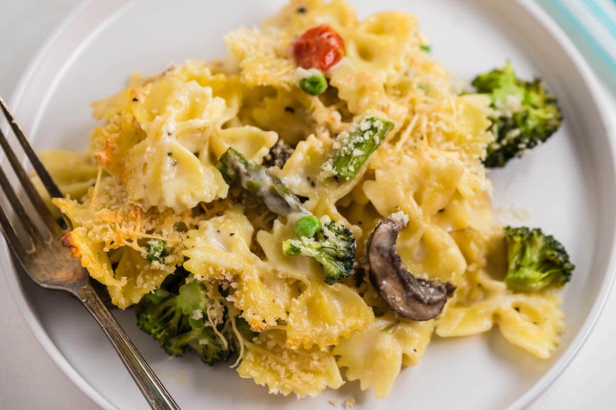 A plate filled with a creamy pasta loaded with vegetables, served with a fork.