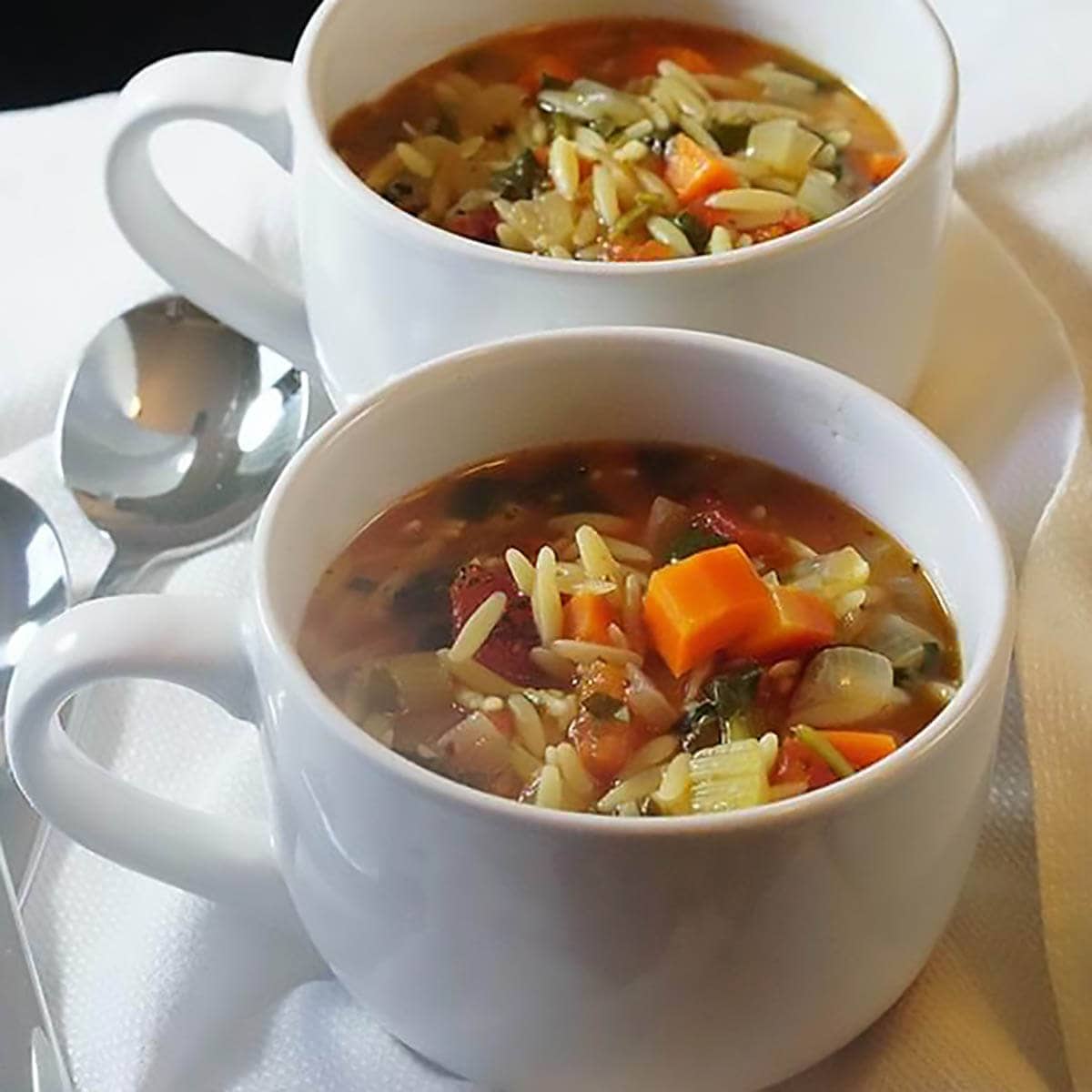 Vegetable Orzo Soup in white bowls with serving spoons.