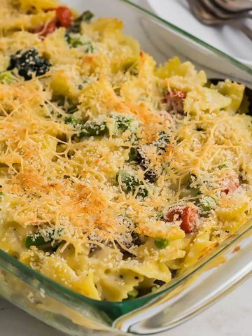 A casserole dish filled with creamy pasta primavera that has a crispy, cheesy topping.
