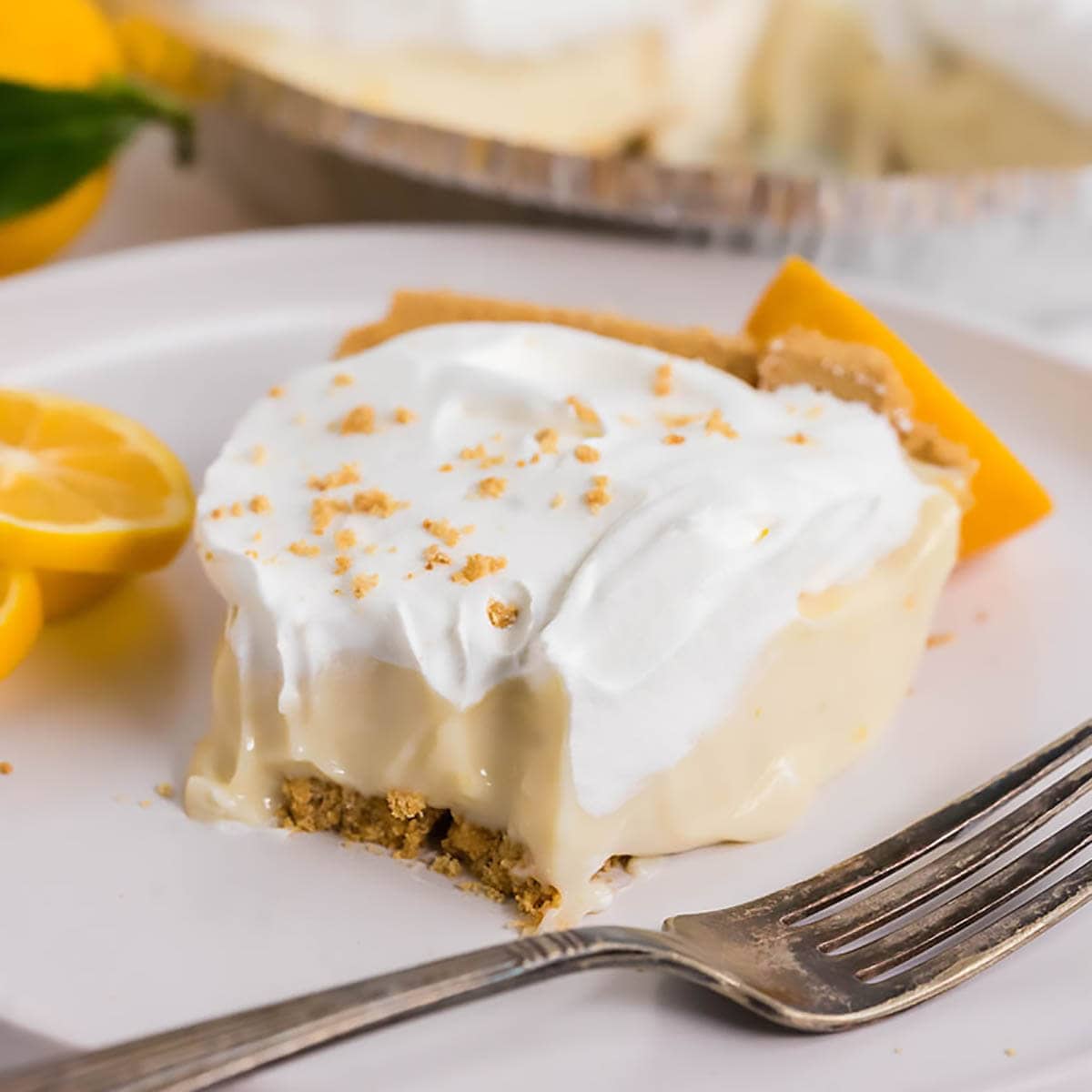 Lemon Icebox Pie on plate with fork. It's garnished with whipped cream and graham cracker crumbs.