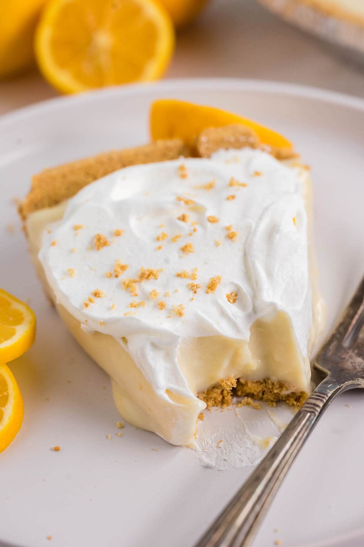 A slice of pie on a plate with a bite taken out of it. It's topped with whipped cream and graham cracker sprinkles.