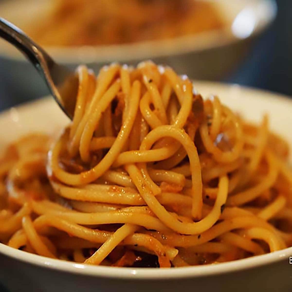 Spaghetti covered in sauce in bowl with fork twirling a big serving of pasta. 