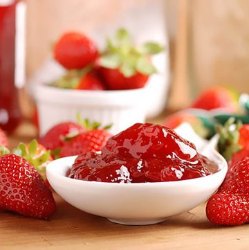 Strawberry jam in a white bowl surrounded by fresh strawberries.