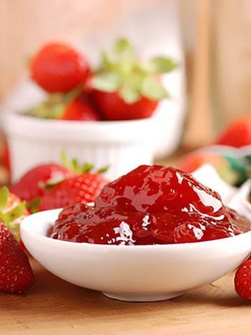 Strawberry jam in a white bowl surrounded by fresh strawberries.