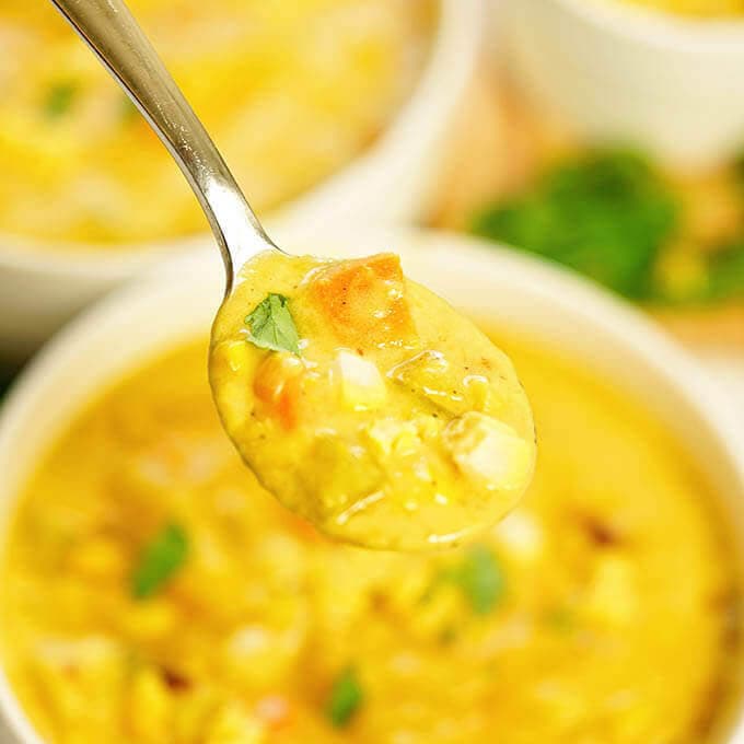 Spoon filled with Vegetarian Corn Chowder over two bowls filled with the soup. 