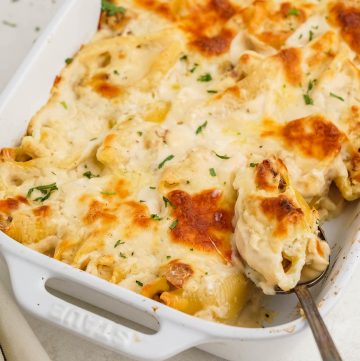Casserole dish filled with Alfredo Stuffed Shells with spoon dishing up a serving.