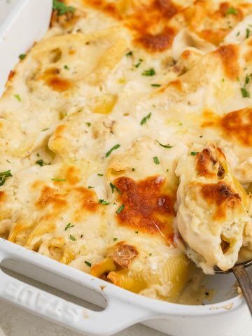Casserole dish filled with Alfredo Stuffed Shells with spoon dishing up a serving.