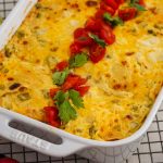 Layered Green Chili Chicken Enchilada Casserole in dish garnished with cilantro and tomatoes.