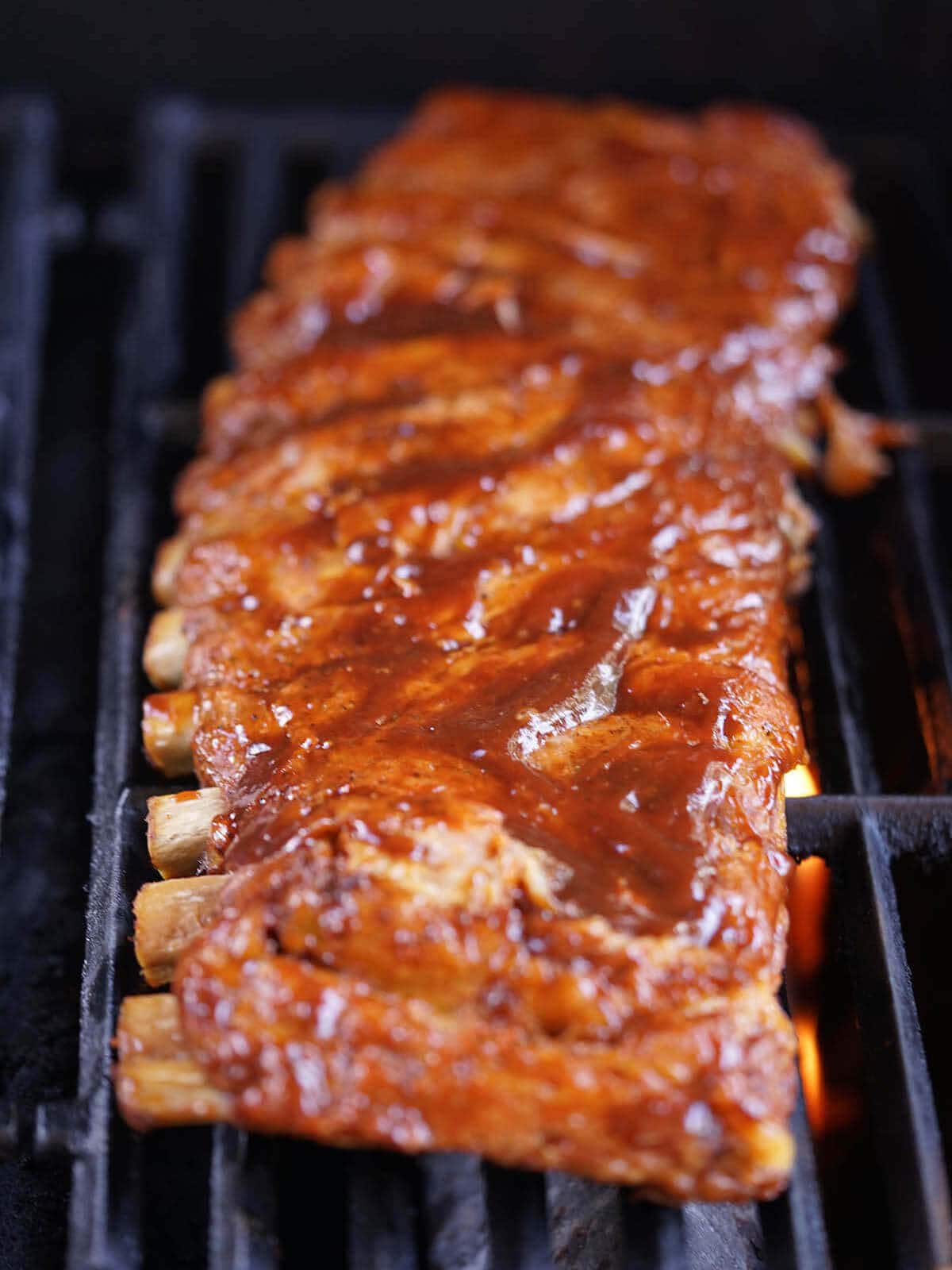 Cooked ribs on the grill slathered with sauce.